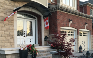 Tinted polycarbonate awning installed over a front door of the canadian contemporary house' entrance with seasonal flags softly mounted on the brackets